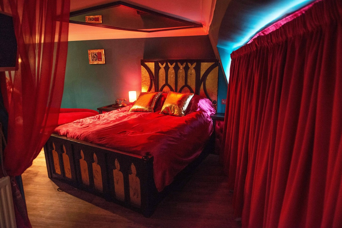Ein Schlafzimmer mit einem Bett, Vorhängen, einem Nachttisch und einem Bild an der Wand.