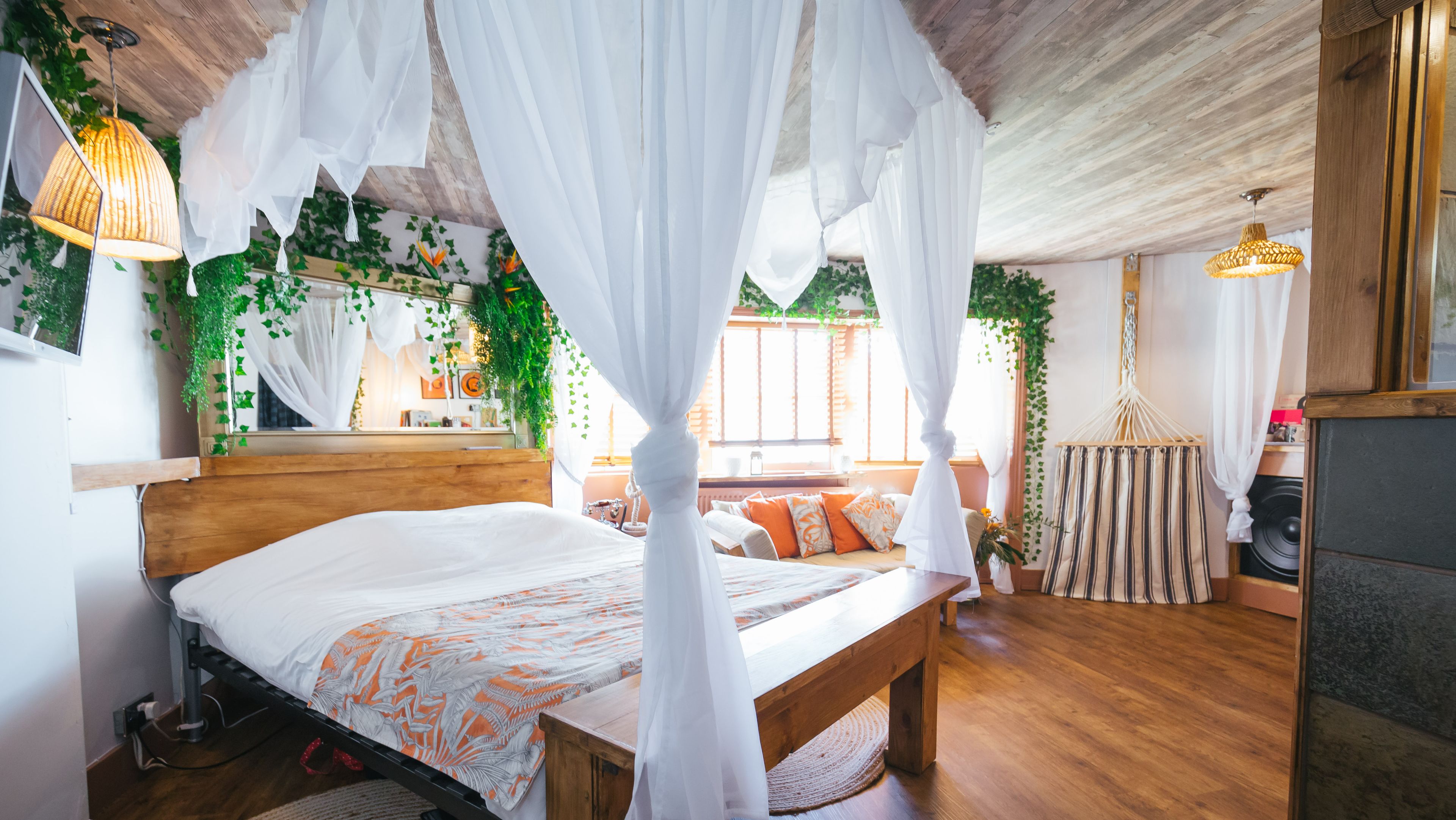A bedroom with a wooden bed, white canopy, and green plants.