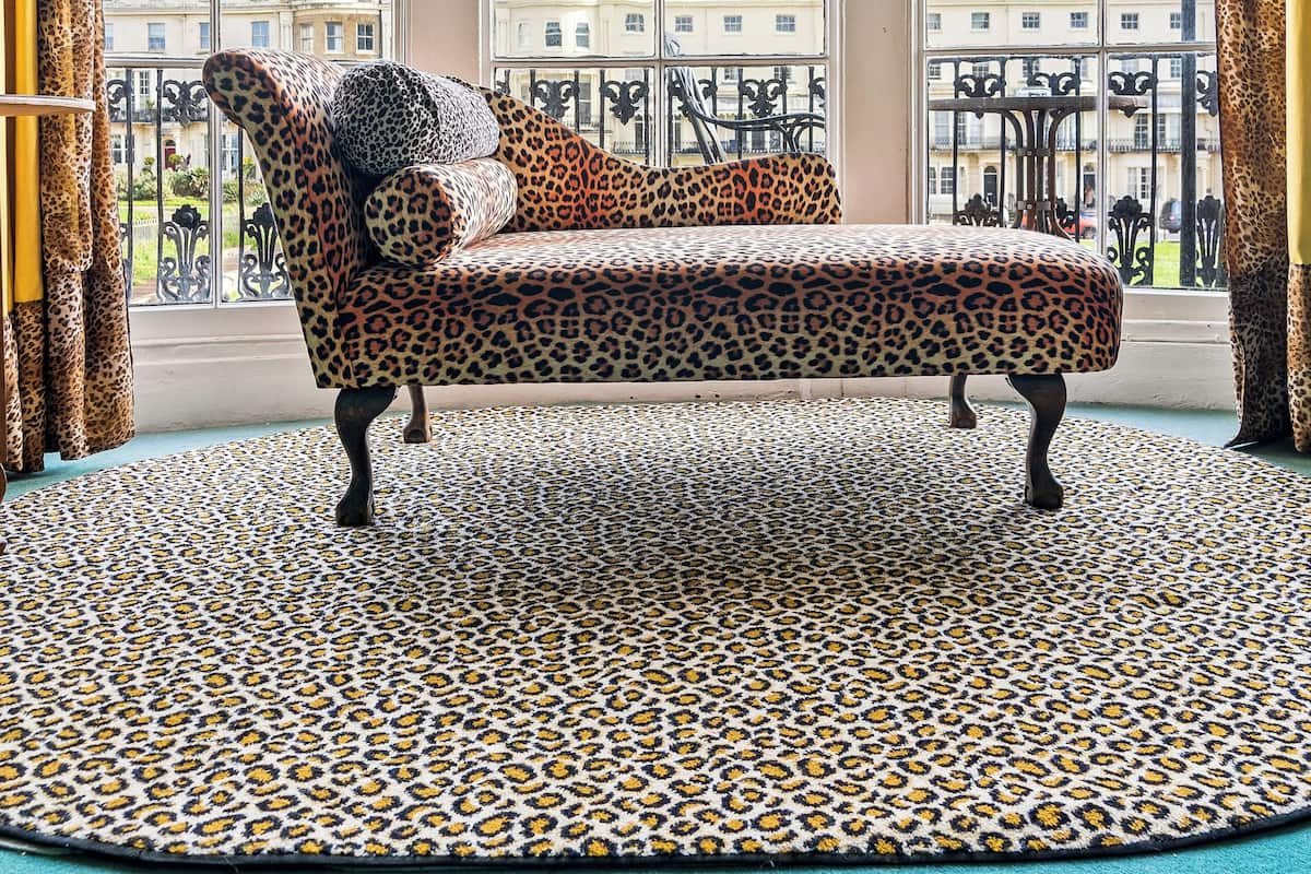 Ein Zimmer mit einer gepolsterten Couch im Leopardenmuster, großen Fenstern und einem gemusterten Teppich.
