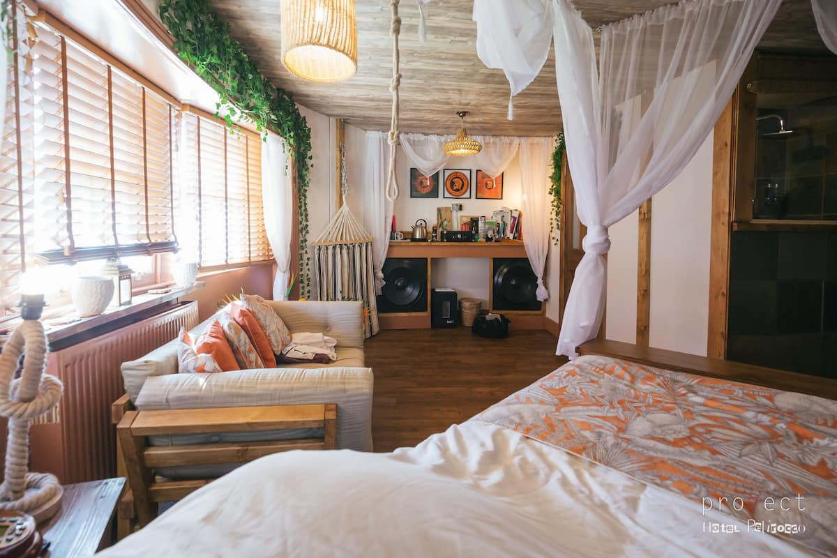 Ein gemütliches Schlafzimmer mit einem Bett, einer hölzernen Bank, einem Schreibtisch mit Stuhl und einem Fenster mit Jalousien.