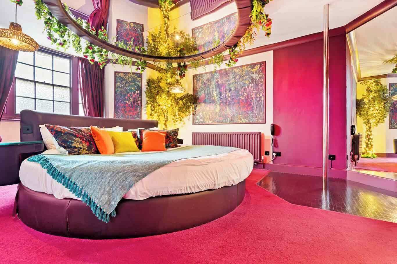 A modern bedroom with a curved bed, vibrant red walls, and a large mirror.