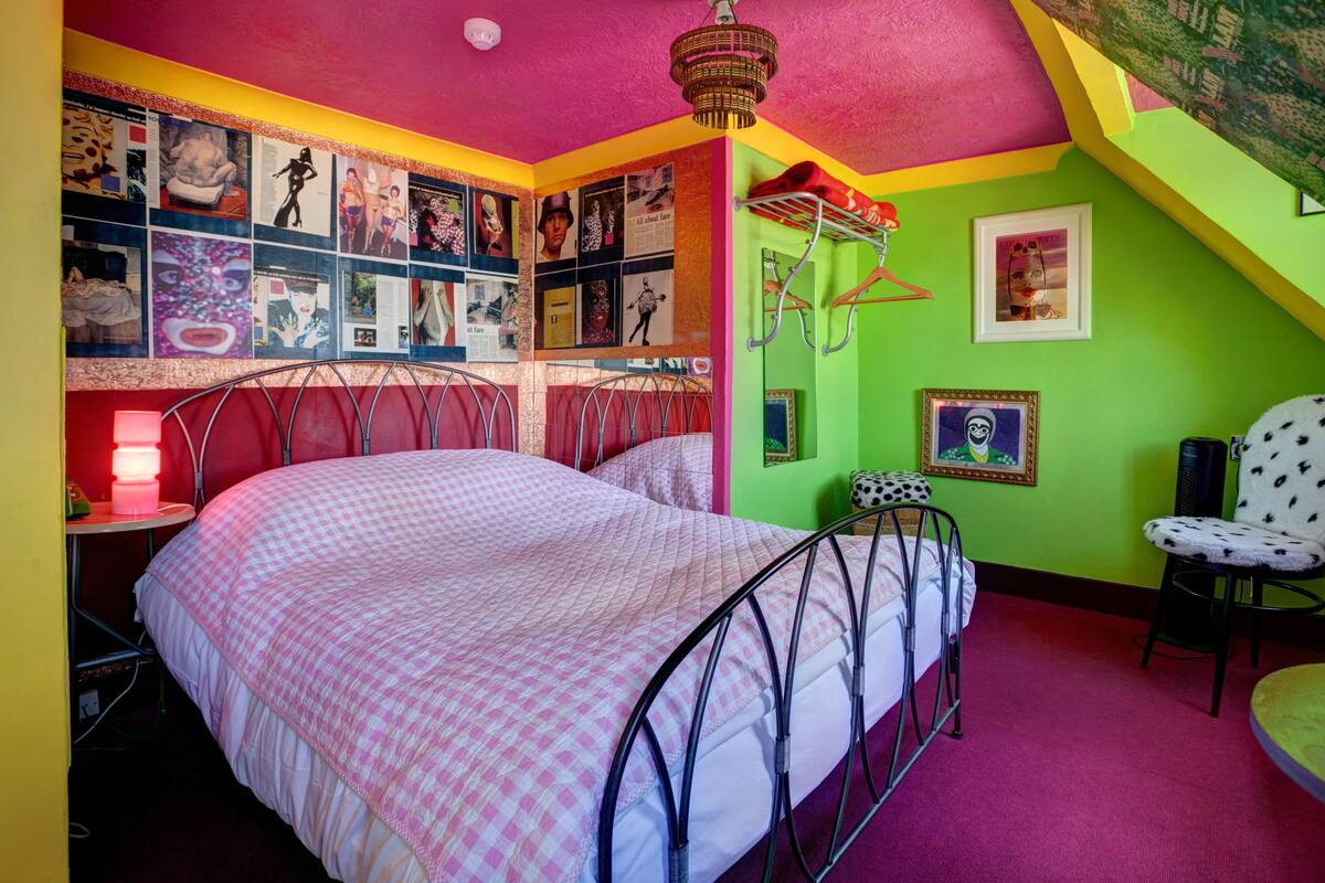 Ein helles Schlafzimmer mit einem Bett, einer Wand voller Poster, einem Hängestuhl und einer roten Lampe.