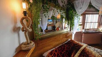 A bedroom with a wooden bed, a rope sculpture, a mirror, and greenery.