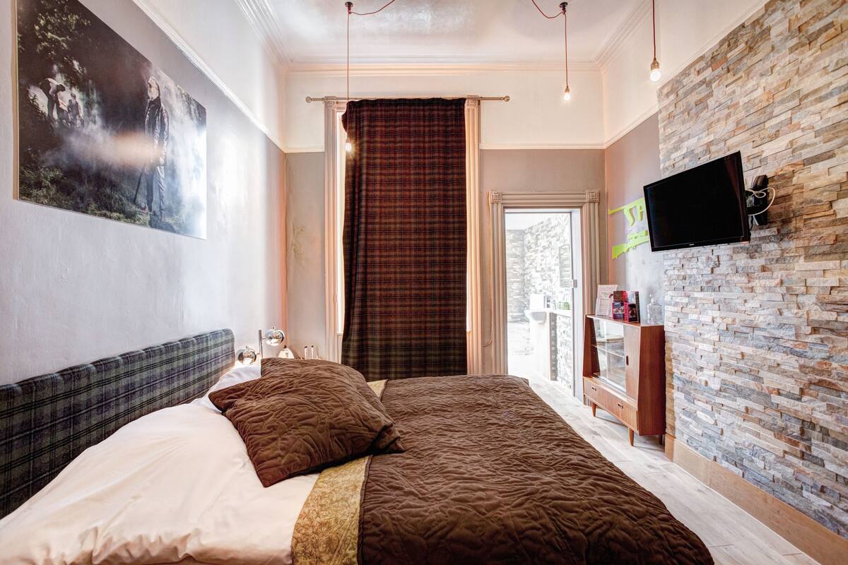 Ein modernes Hotelzimmer mit einem großen Bett, einem Flachbildfernseher an einer Steinwand und Blick ins Freie.