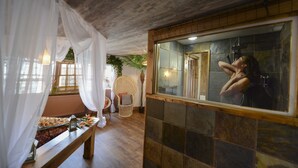 A room with a wooden ceiling, a large mirror, a bench with snacks, and a wicker chair.