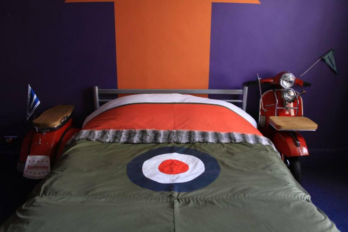 Ein Bett mit einem Ziel-Design auf der Bettdecke, ein rotes Vintage-Motorrad und eine Flagge auf der linken Seite.