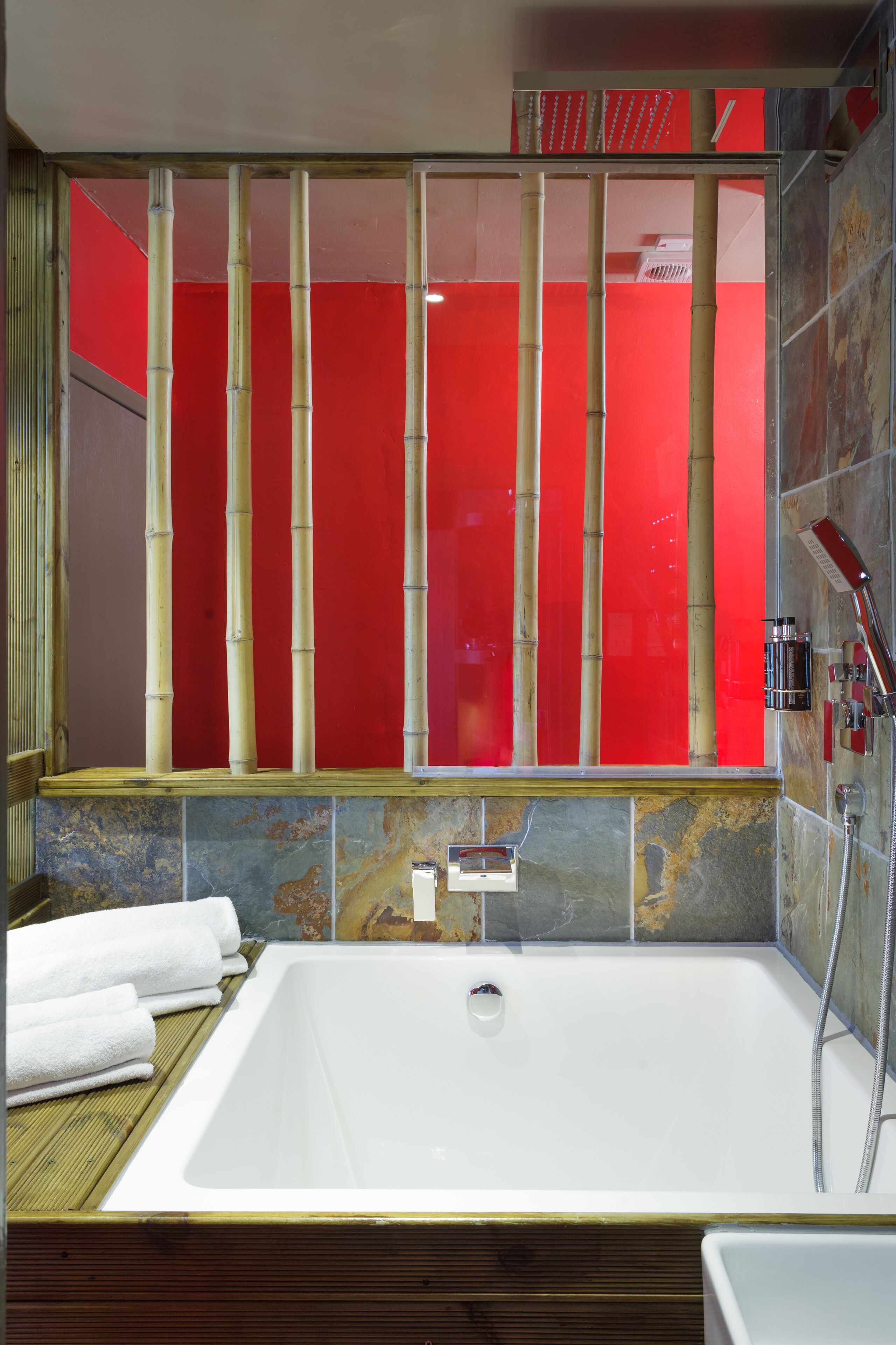 A modern bathroom with a large bathtub, a glass shower enclosure, and a red accent wall.