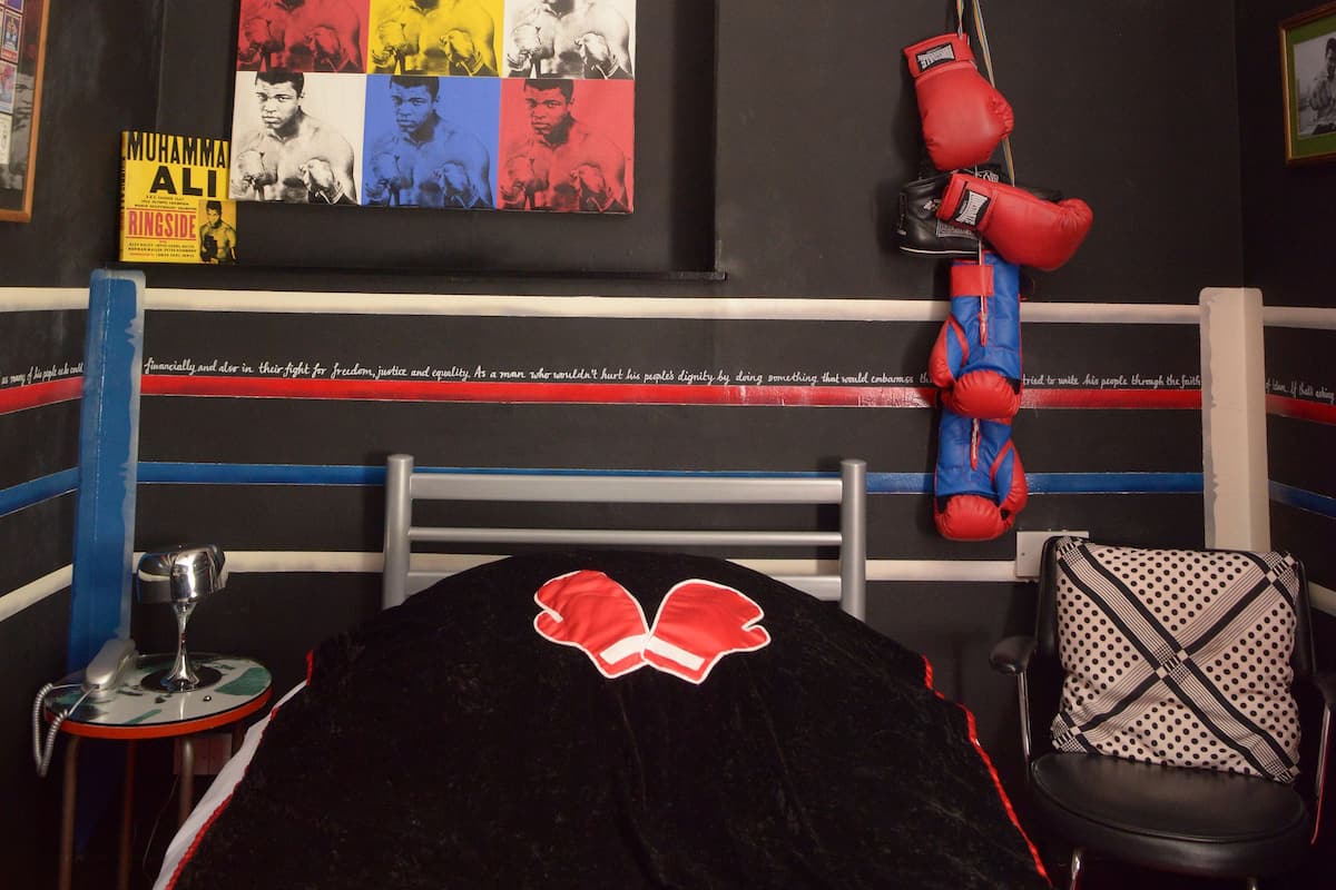 Ein Boxring mit einem Poster von Muhammad Ali, einem roten Boxhandschuh und einem Sandsack.