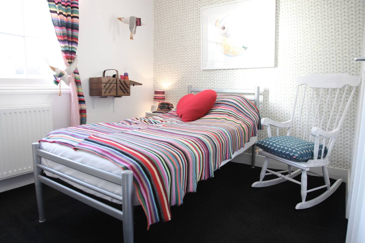 Ein Kinderzimmer mit Bett, Schaukelstuhl und einer an der Wand befestigten Regal mit Spielzeug.