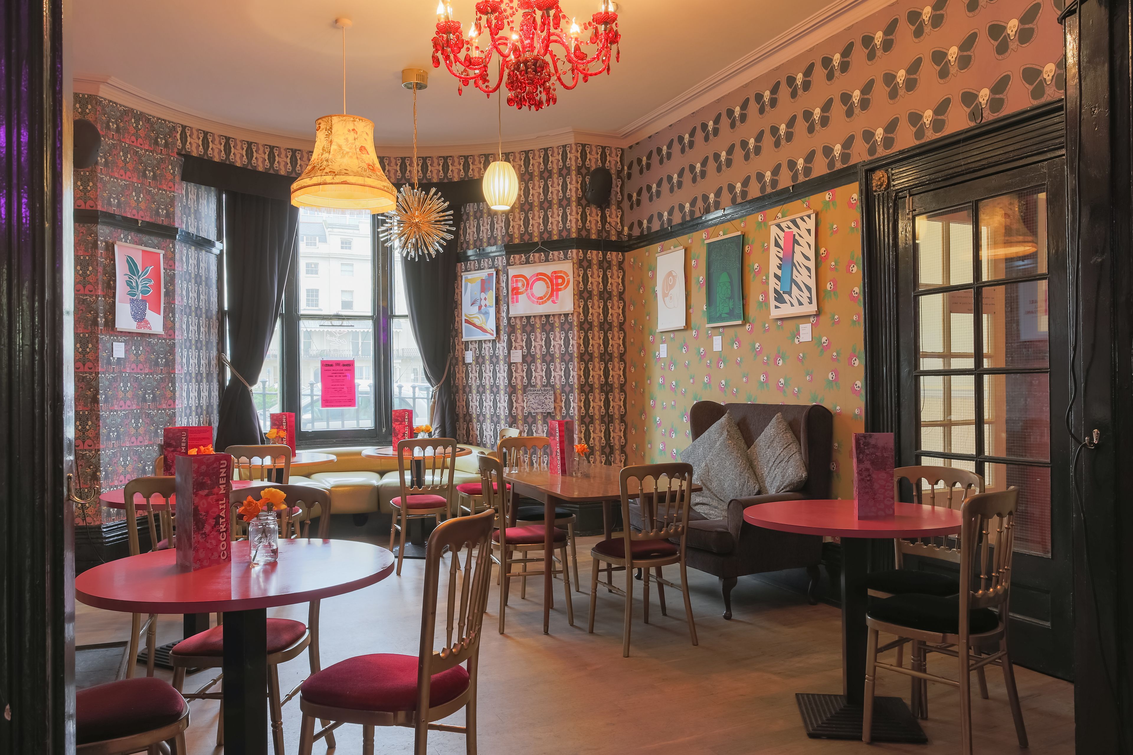 A cozy dining area with patterned wallpaper, a chandelier, and various seating arrangements.