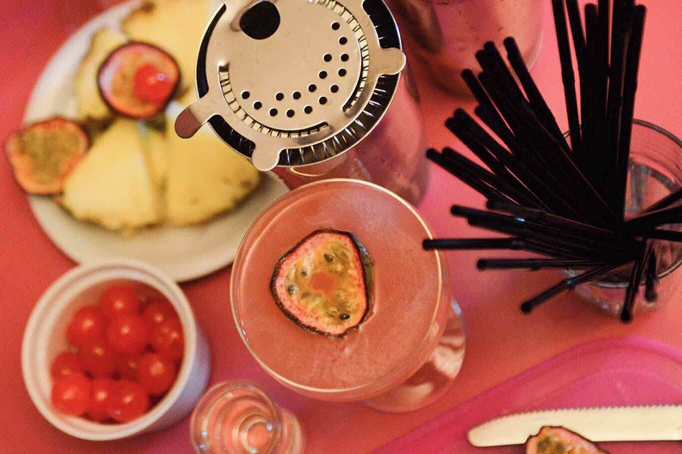 A table with a plate of sliced fruits, a drink with a slice of fruit, a small bowl of cherry tomatoes, and a decorative item.