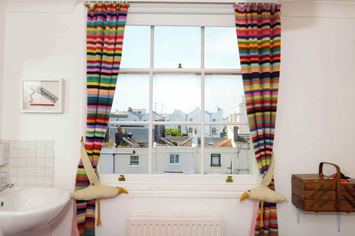 A bathroom with a window, striped curtains, a sink, a radiator, and a wooden chest of drawers.