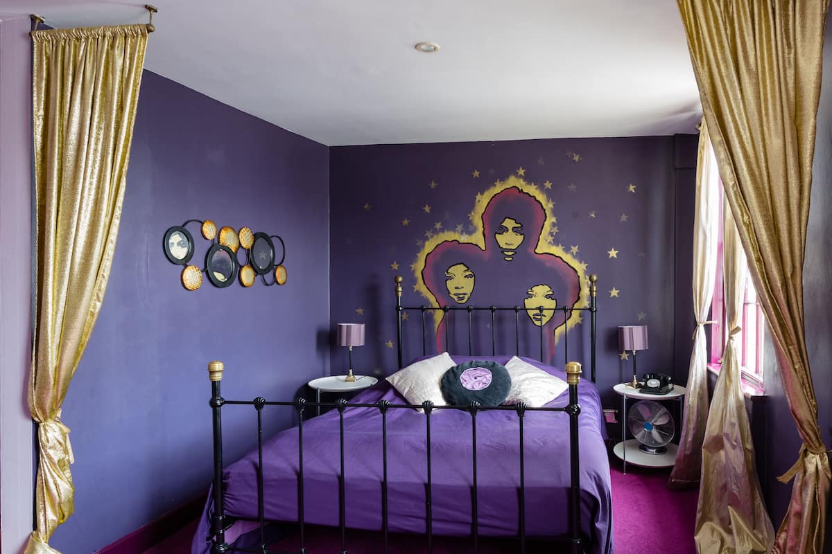 Ein Schlafzimmer mit einem violetten Bett, goldenen Vorhängen, einer Wanduhr und einem Sternenwandbild.