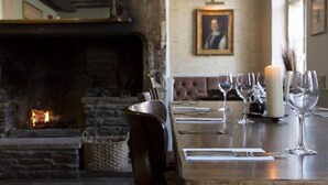 A dining area with a fireplace, a framed portrait on the wall, and a table set for a meal. - Red Lion - B&B (Chippenham)