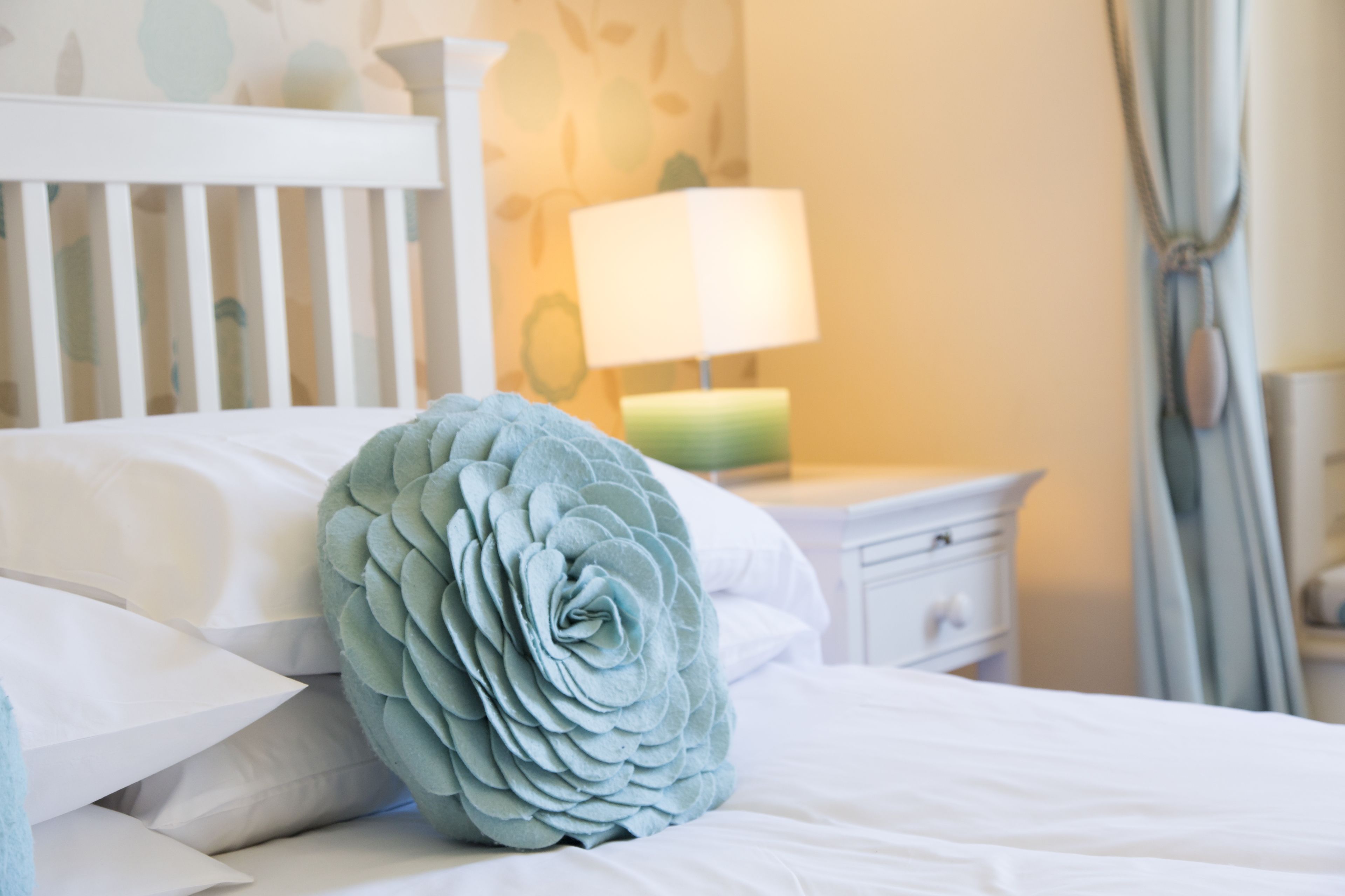 A neatly made bed with a decorative pillow, a bedside lamp, and a white nightstand.