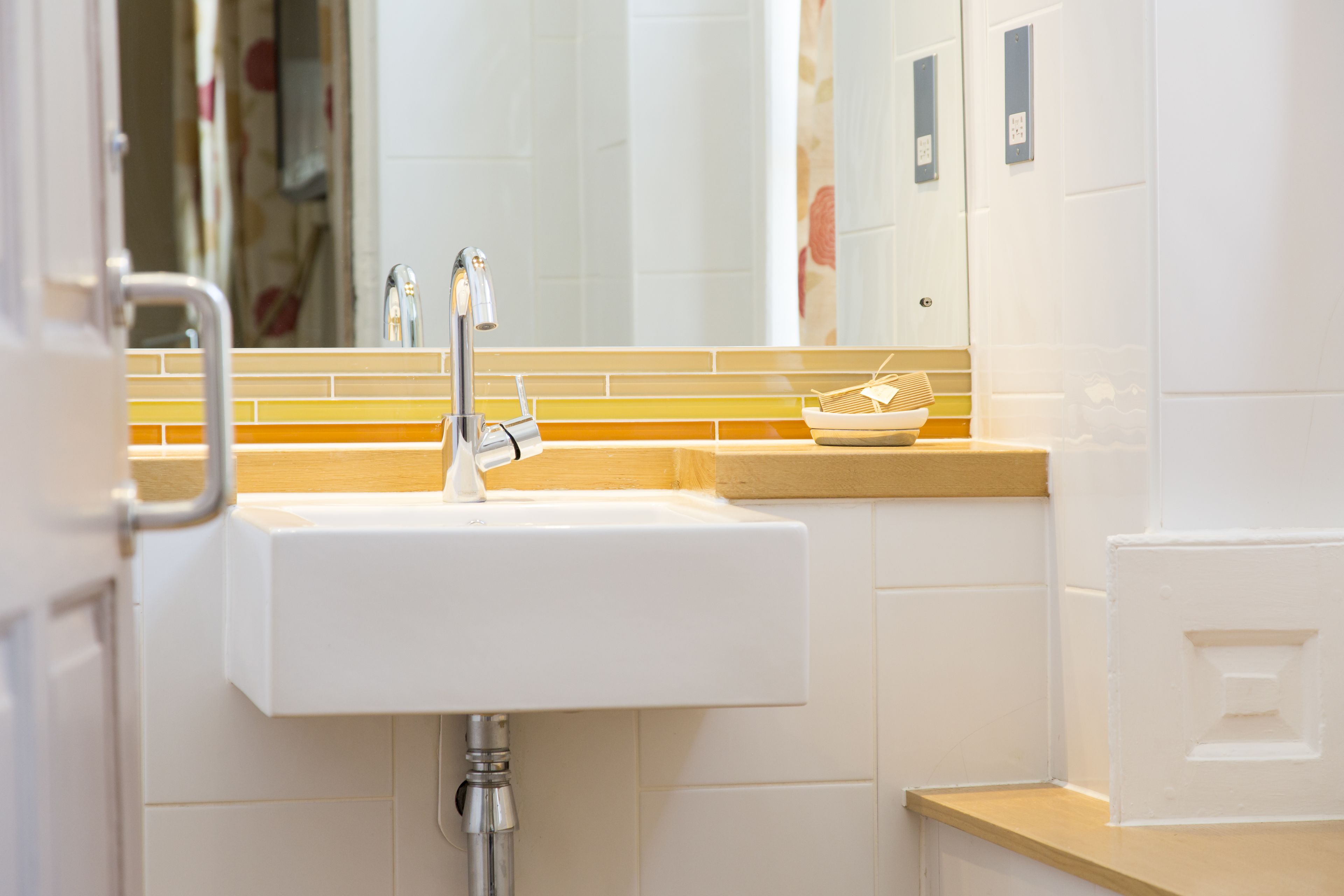 Un baño con lavamanos blanco, espejo y barra para toallas.