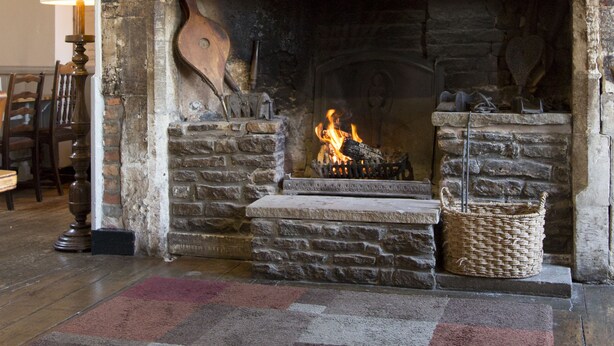 A fireplace with a stone arch, a fire burning inside, and a rug on the floor. - Red Lion - B&B (Chippenham)