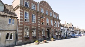 A traditional brick building with a sign reading "The Red Lion." It features multiple windows, some with flower baskets, and a clear, sunny sky. - Red Lion - B&B (Chippenham)