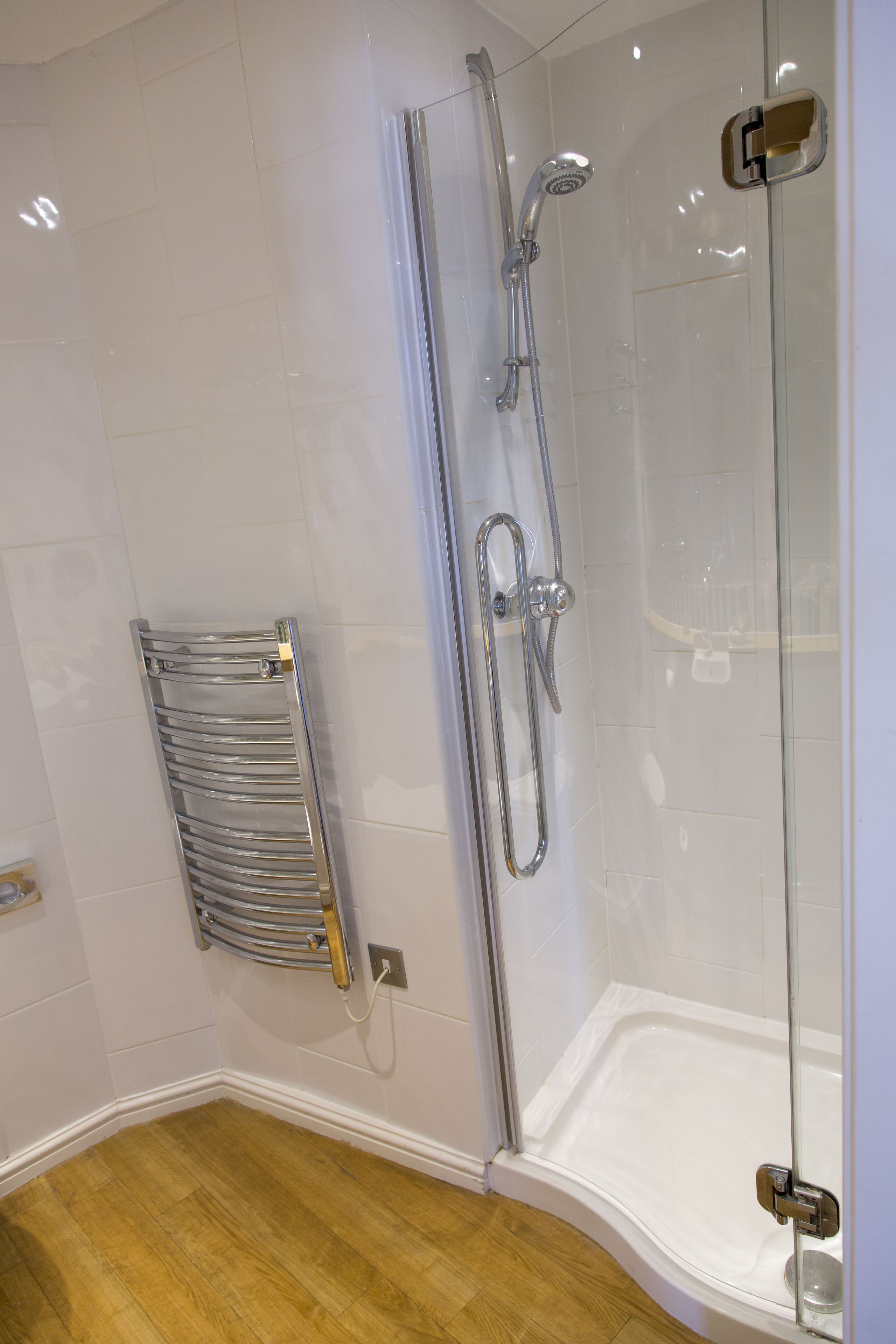 Un baño moderno con ducha de vidrio, toallero de cromo y piso de madera.