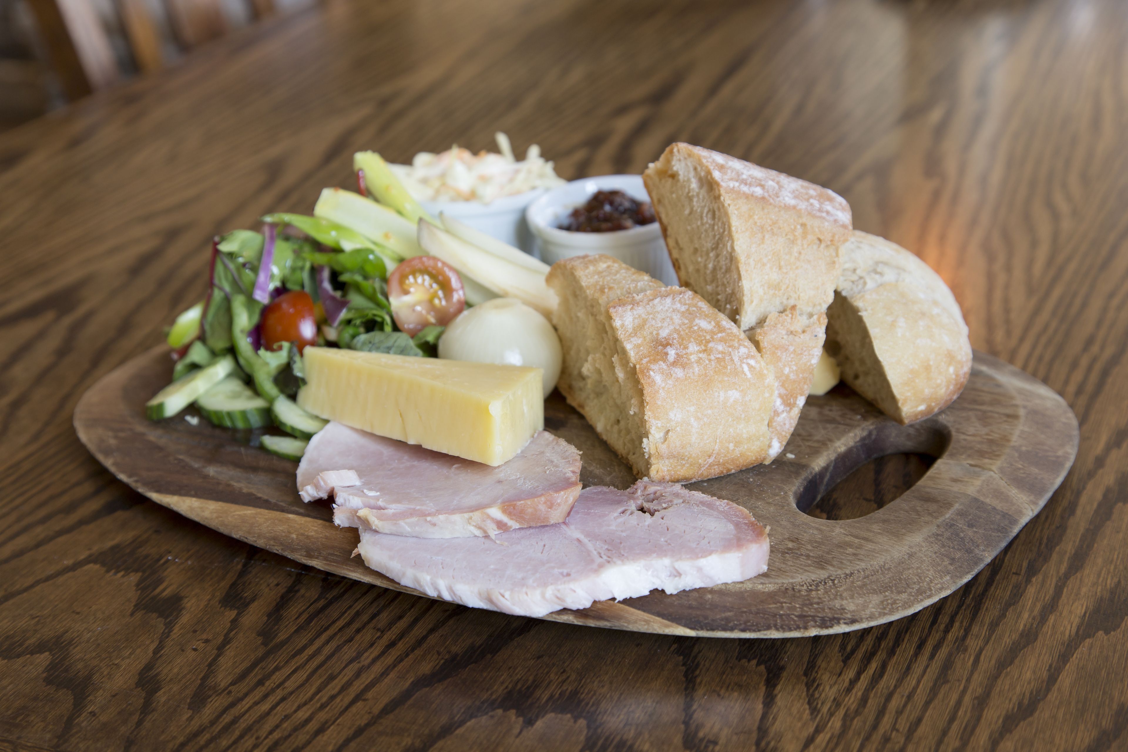 Ein Holzbrett mit Schinken, Käse, Brot und Salat auf einem Holztisch.