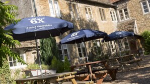 A stone building with a traditional facade, outdoor wooden tables, and umbrellas with text. - Red Lion - B&B (Chippenham)