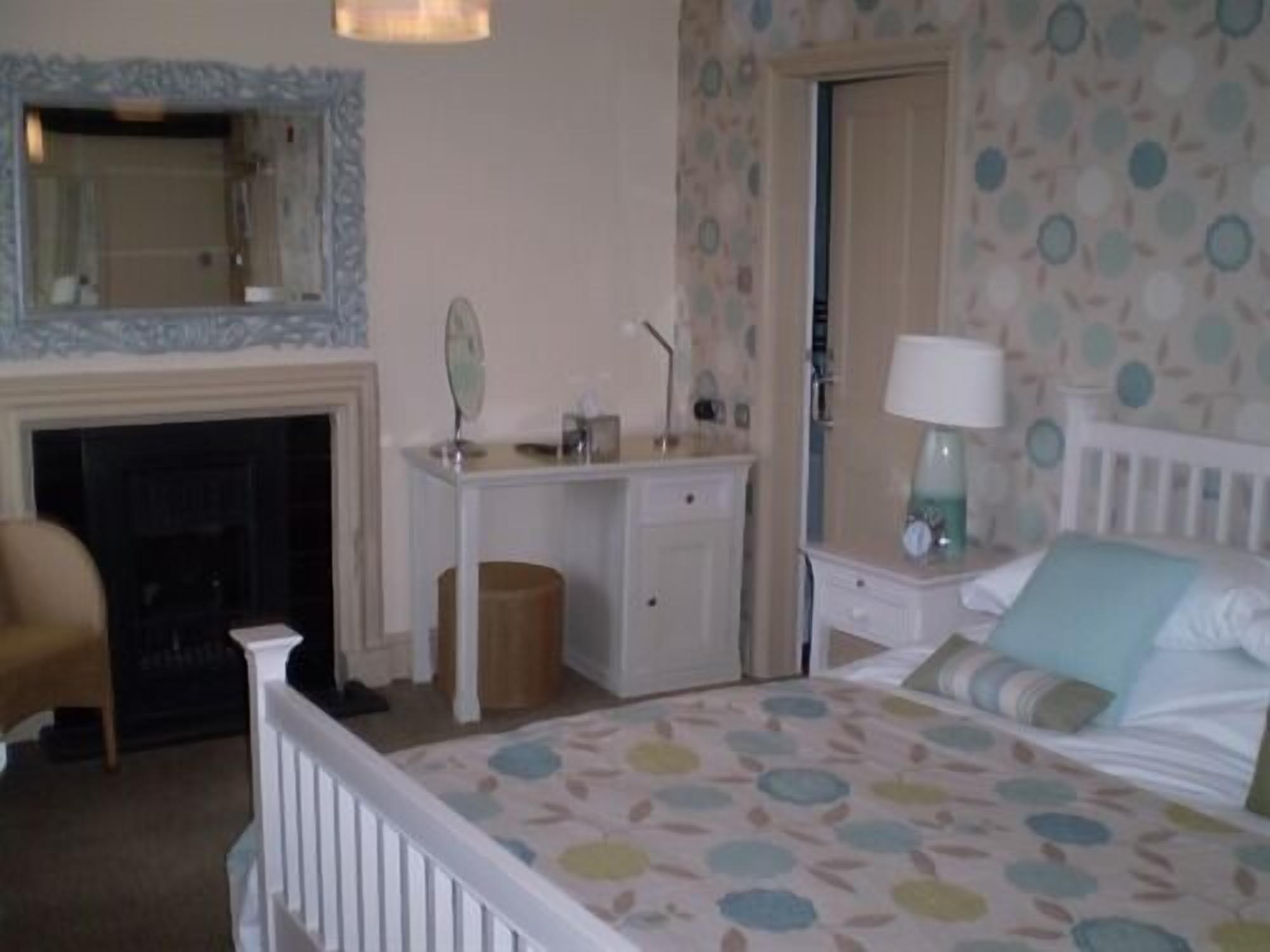 A bedroom with a bed, a dresser, a mirror, a lamp, and a fireplace.