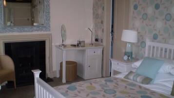 A bedroom with a bed, a dresser, a mirror, a lamp, and a fireplace.