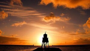 La silhouette d’un phare se détachant sur le ciel d’un coucher de soleil.