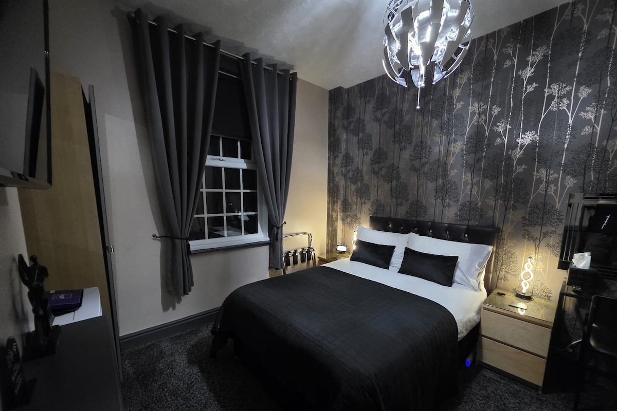 Slaapkamer met een bed, gordijnen, een nachtkastje, een lamp en een muur met een boommotief.