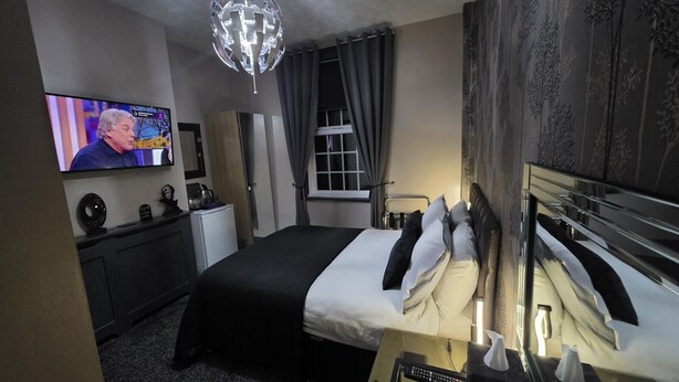 Une chambre d’hôtel équipée d’un lit, d’une télévision, d’un bureau, d’une chaise, d’une armoire et d’un lustre.