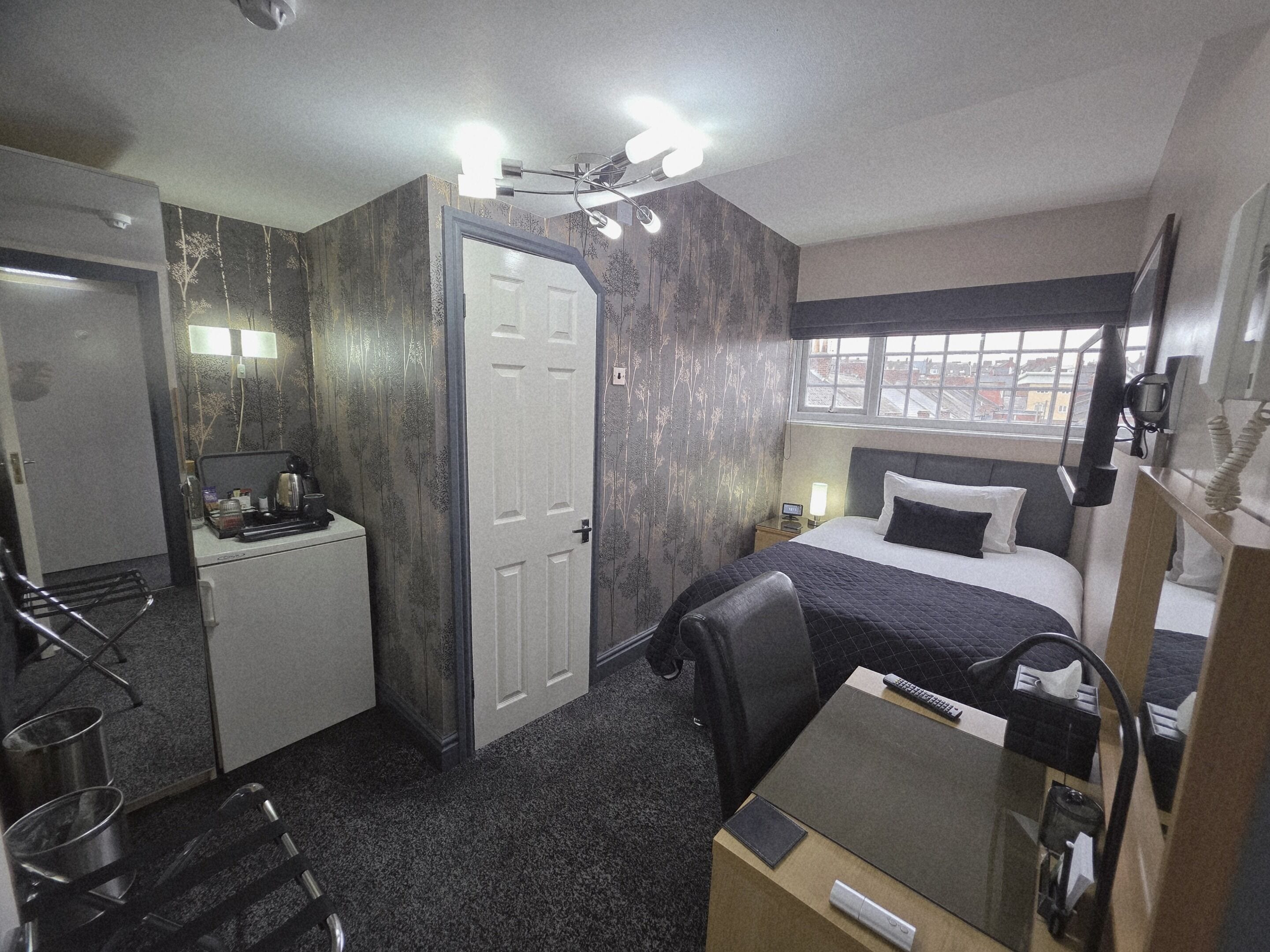 Een kleine hotelkamer met een bed, bureau, stoel en een klein kitchenette.