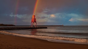 Une plage avec un phare rouge et un arc-en-ciel.