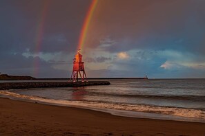 Een strand met een rode vuurtoren en een regenboog.