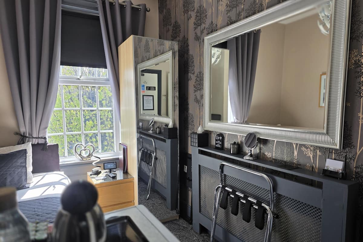 A hotel room with a bed, a desk with a telephone, a mirror, and a radiator.