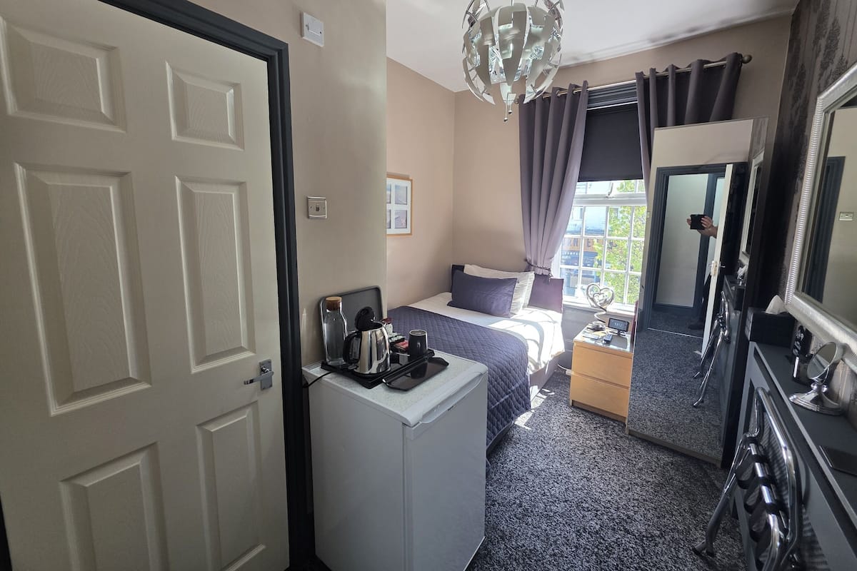 Een hotelkamer met een bed, een bureau, een spiegel, een kroonluchter en een raam met gordijnen.