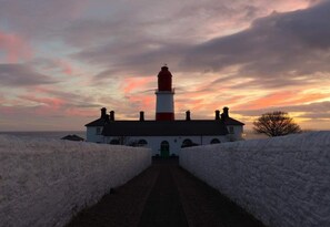 A lighthouse with a brick pathway leading to it, surrounded by snow-covered walls.