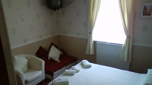 A hotel room with a bed, a chair, a TV, and a window with curtains. - Brampton Guest House (Paignton)