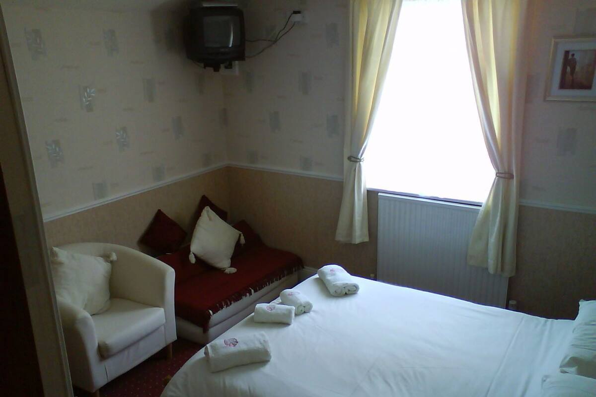 Une chambre d’hôtel avec un lit, une chaise, une télévision et une fenêtre avec des rideaux.