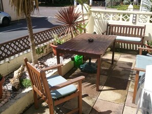 An outdoor patio with a wooden table and chairs, surrounded by potted plants and a decorative fence. - Brampton Guest House (Paignton)