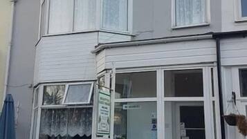 Un edificio de varios pisos con acceso a nivel de calle, un ventanal visible y un pequeño espacio exterior con mesas y sillas.
