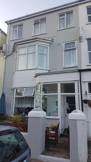 A multi-story building with a ground-level entrance, a visible window, and a small outdoor seating area. - Brampton Guest House (Paignton)