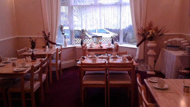 A dining area with multiple wooden tables and chairs, arranged in a semi-circle. - Brampton Guest House (Paignton)