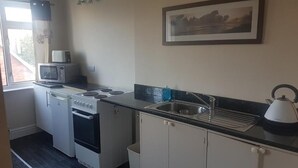 A compact kitchen with a microwave, stove, oven, sink, and a kettle. - Brampton Guest House (Paignton)