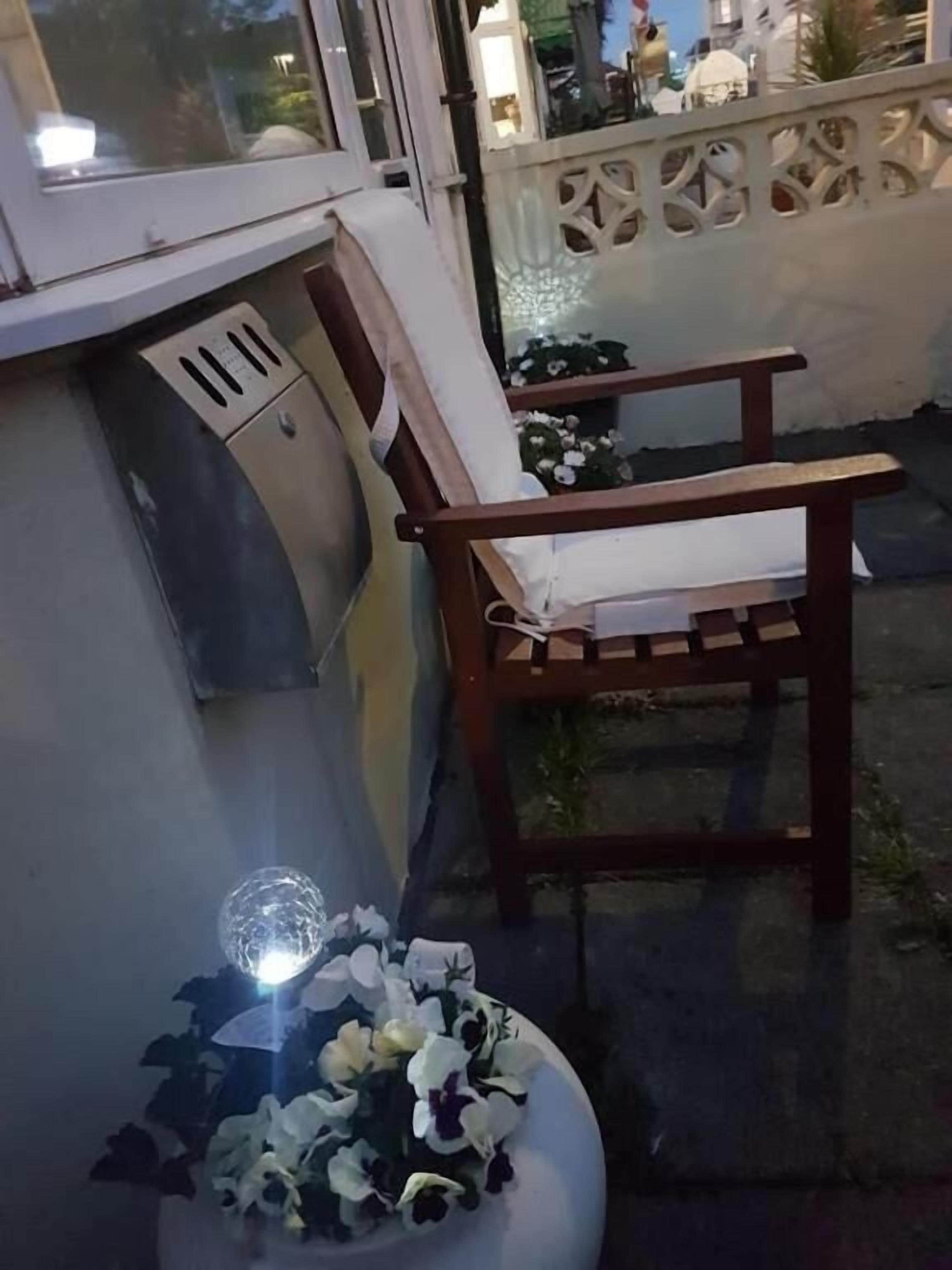 Un banco de madera con cojín, una planta en maceta con flores y una ventana con rejilla.