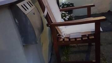 Un banco de madera con cojín, una planta en maceta con flores y una ventana con rejilla.