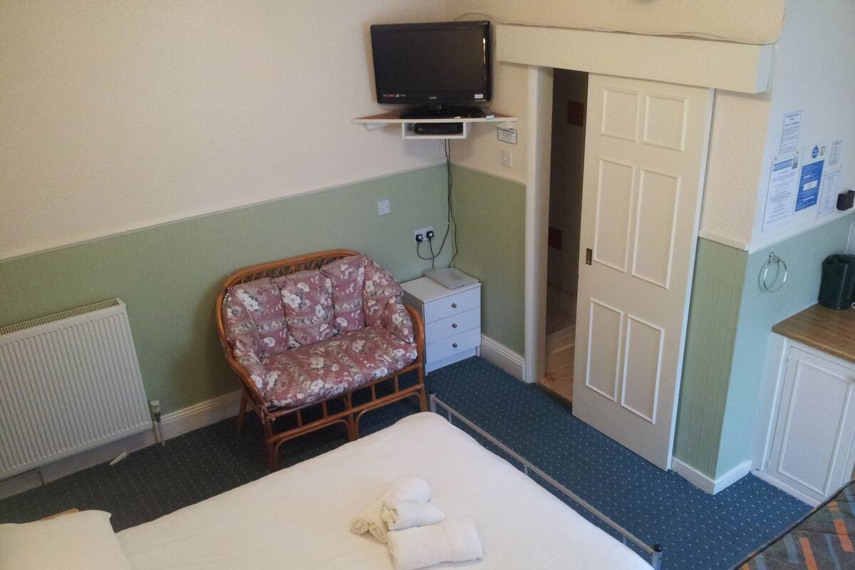 Une chambre d’hôtel avec un lit, une chaise, une petite table, un téléviseur et une porte.