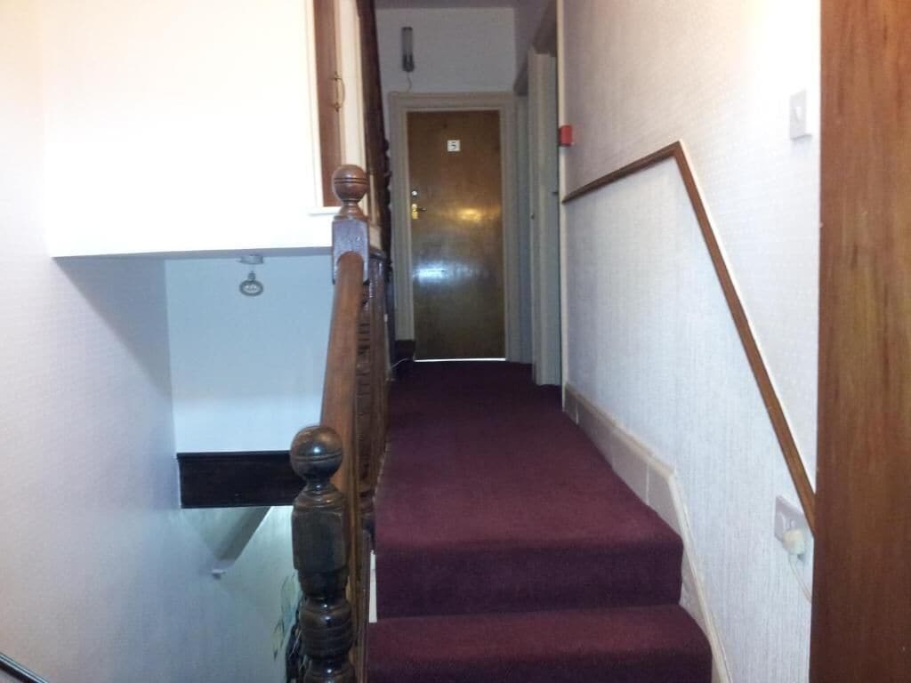 A staircase with a wooden handrail and a red carpeted landing.