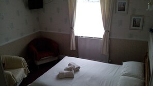 A hotel room with a single bed, a chair, a television mounted on the wall, and a window with curtains. - Brampton Guest House (Paignton)