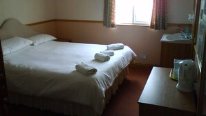 A hotel room with a bed, a bedside table, a window with curtains, and a bathroom with a sink and mirror. - Brampton Guest House (Paignton)
