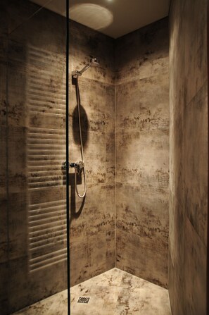 A shower with a glass door, a handheld showerhead, and a wall-mounted control panel.